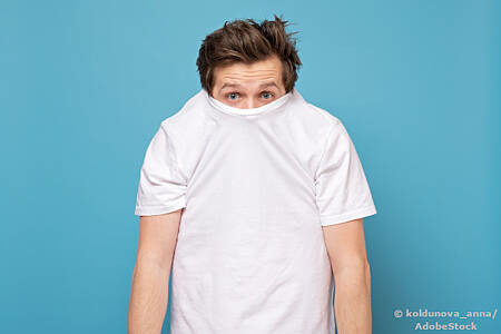 Ein junger Mann versteckt sein Gesicht in seinem T-Shirt. Foto: AdobeStock/koldunova_anna