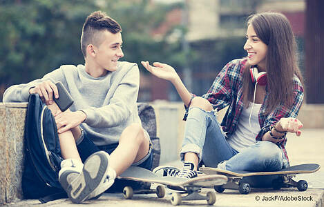 Ein Junge und ein Mädchern, die auf Skateboards sitzen. Foto: JackF/AdobeStock. 