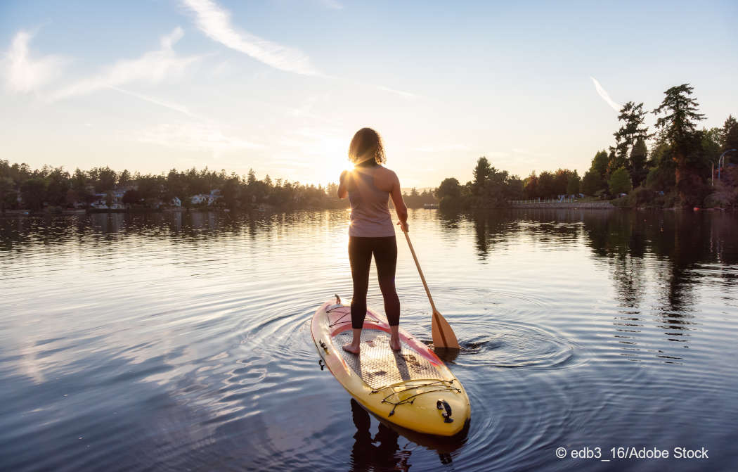 Eine SUP-Paddlerin rudert dem Sonnenuntergang entgegen. Foto: edb3_16/Adobe Stock.